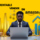 Hombre con traje trabajando en un portátil rodeado de cajas, monedas y gráficos de crecimiento, con el texto '¿Es rentable vender en Amazon?' sobre fondo amarillo